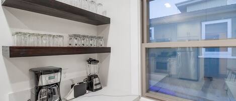 A kitchen with two coffee makers, a blender, and glass jars on shelves.