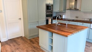 A kitchen with light blue cabinets, a wooden island with a sink, and stainless steel appliances. - Churchmount Holiday Home Roundwood (Roundwood)
