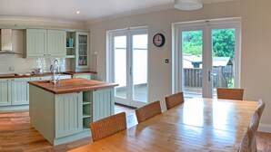 A spacious kitchen with a central island, a dining area with a long table and wicker chairs, and large sliding glass doors leading to an outdoor area. - Churchmount Holiday Home Roundwood (Roundwood)