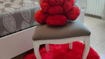 A chair with a red cushion in a room with a white bed and a red furry rug.