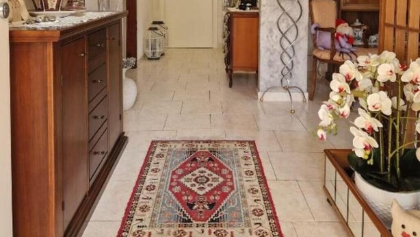 A hallway with a wooden cabinet, a mirror, a patterned rug, and a potted plant with flowers. - Delightful Apartment Tourist Rental (Lonigo)