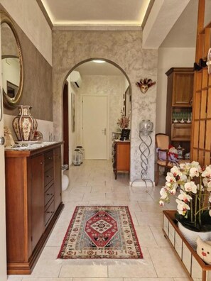 Un couloir avec une armoire en bois, un miroir, un tapis à motifs et une plante en pot ornée de fleurs.