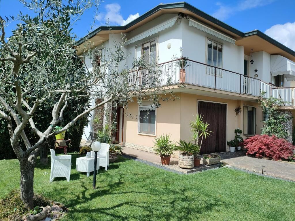 Une maison à deux étages avec un balcon, une porte d’entrée et un petit jardin agrémenté de chaises et de plantes en pot.