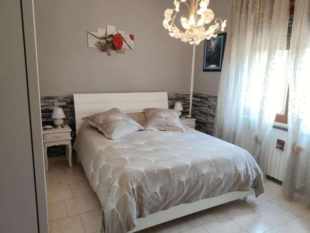 Ein Schlafzimmer mit Bett, Nachttischen, einer Chandelüster und einem Fenster mit Vorhängen.