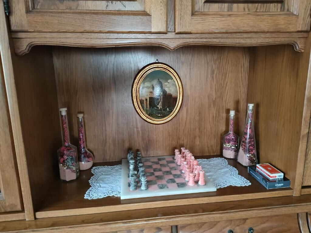 Un meuble en bois orné d’un jeu d’échecs, d’un tableau encadré et de bouteilles décoratives.