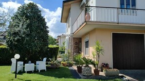 A two-story house with a balcony, a garage, and a well-maintained garden with potted plants and outdoor furniture. - Delightful Apartment Tourist Rental (Lonigo)