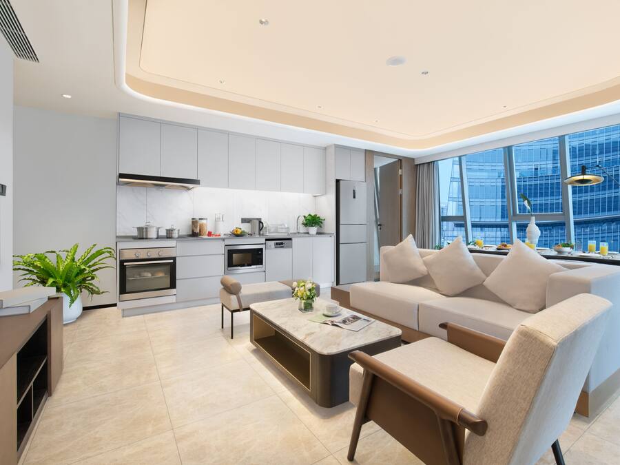Una cocina moderna con armarios blancos, horno empotrado y un área de comedor con sofá blanco y mesa de centro.