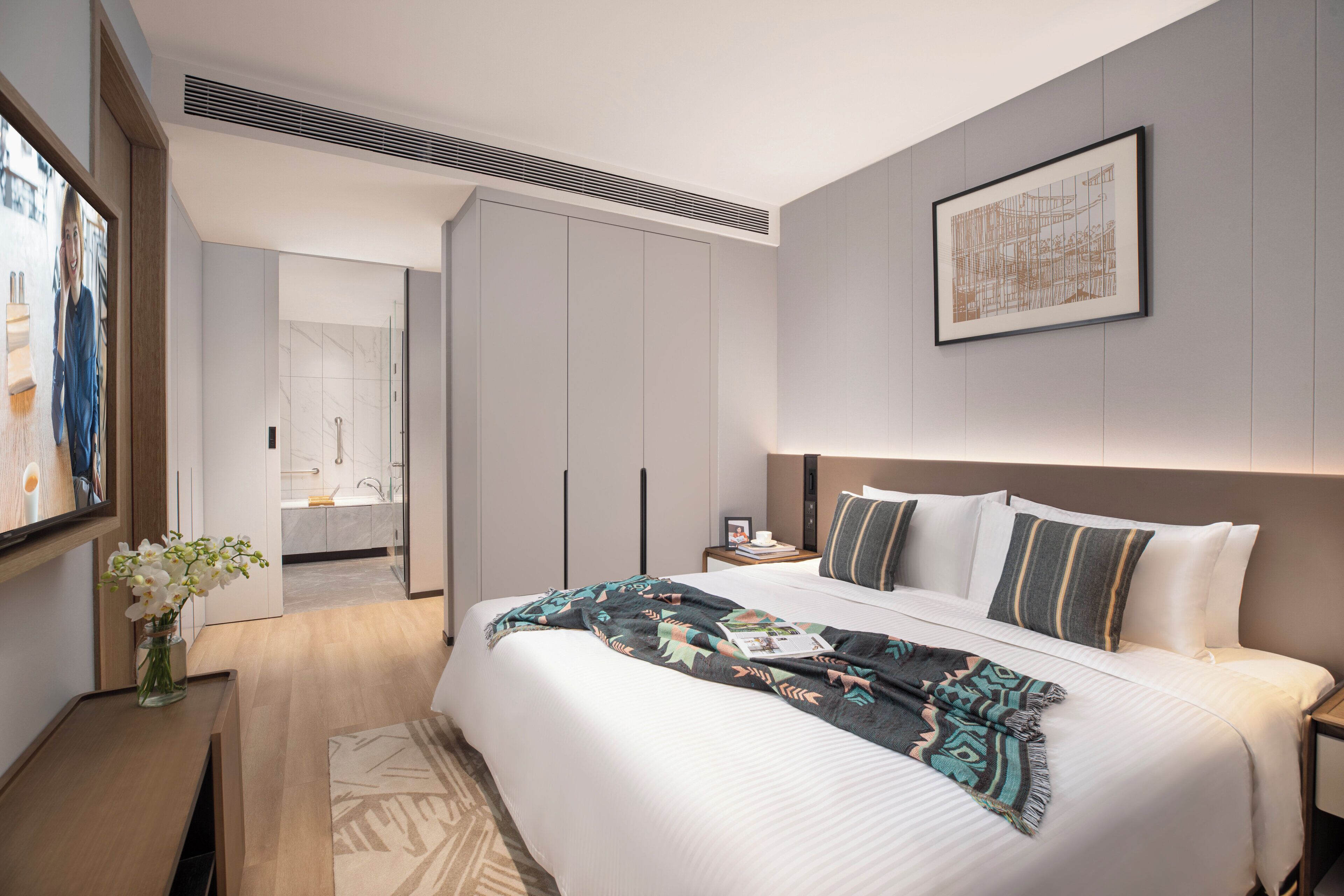 A modern hotel room with a large bed, a bedside table, a nightstand, and a wall-mounted artwork.