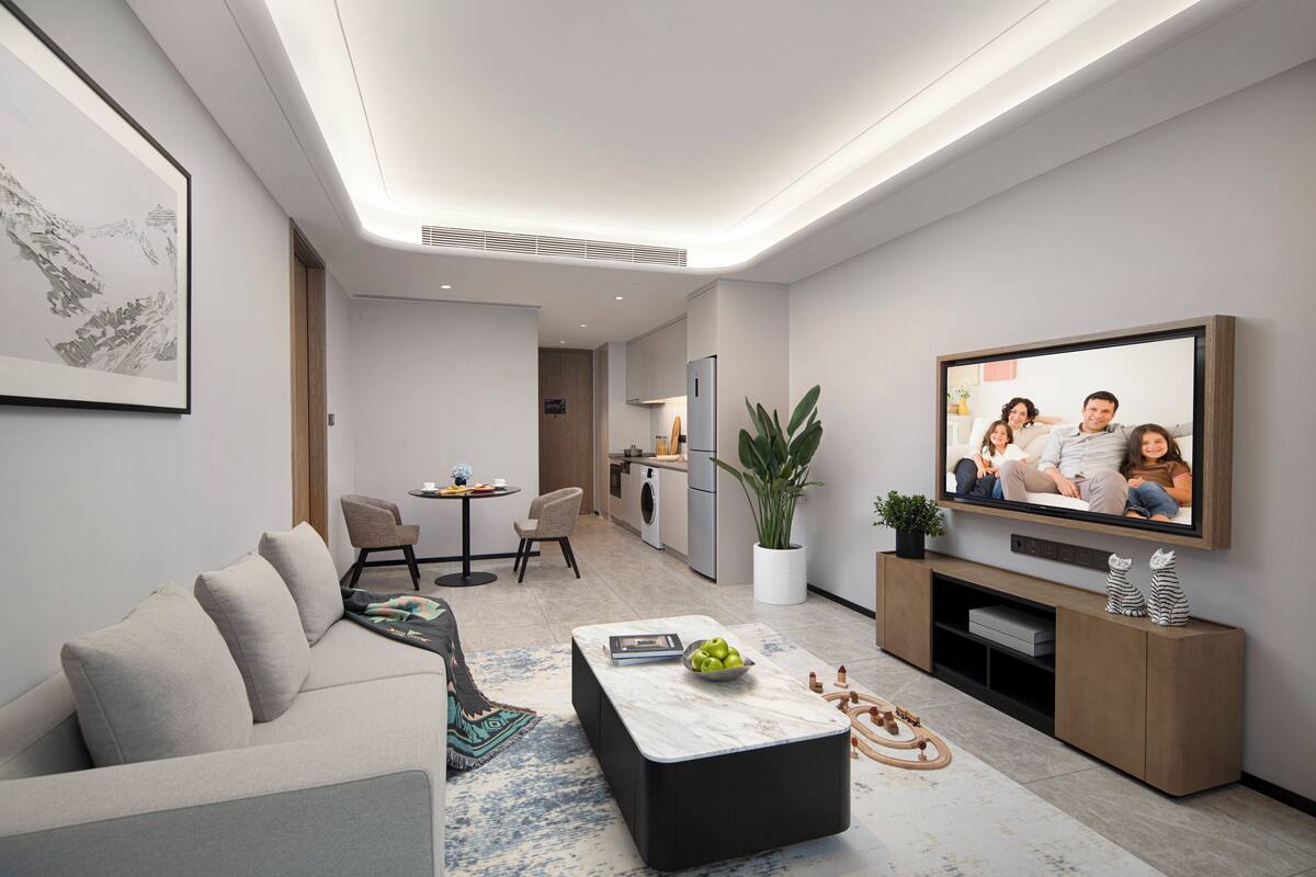 A modern living room with a sofa, coffee table, TV, and a dining area with chairs and a table.