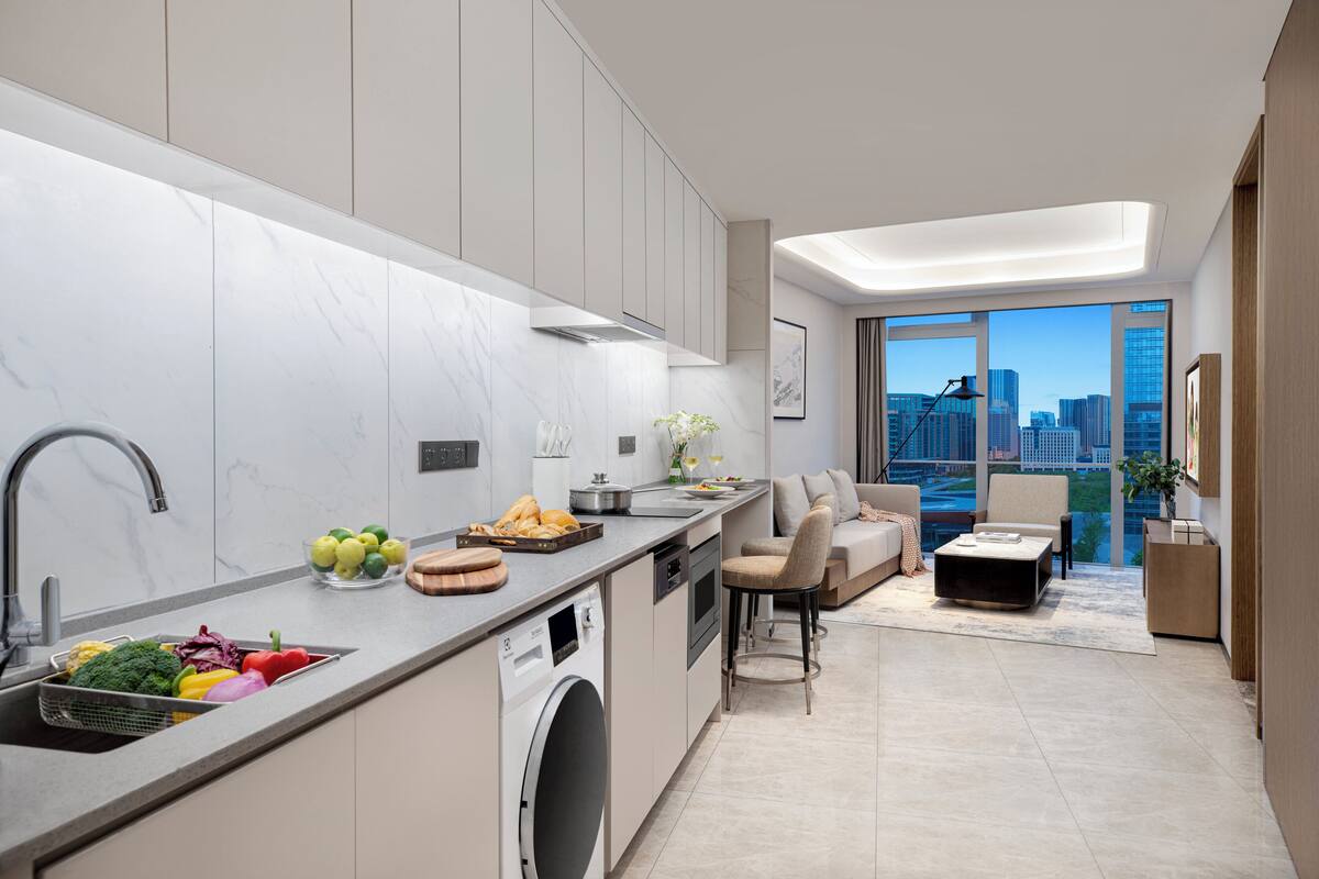 A modern kitchen with a built-in dishwasher, a dining area with a sofa and chairs, and a large window offering a city view.