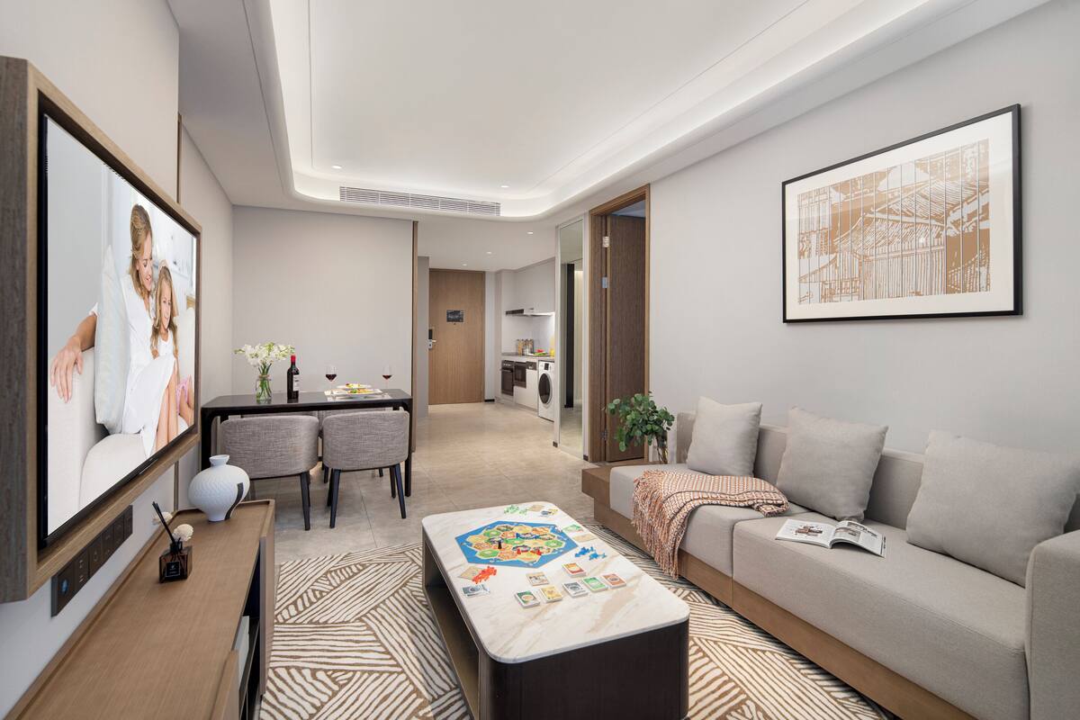A modern hotel room with a dining area, a sofa, a coffee table with a board game, and a large framed artwork on the wall.