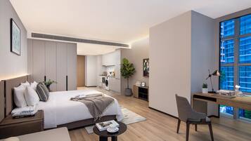 A modern hotel room with a large bed, a desk, a chair, and a view of the city through large windows.