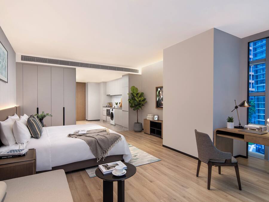 A modern hotel room with a large bed, a desk, a chair, and a view of the city through large windows.