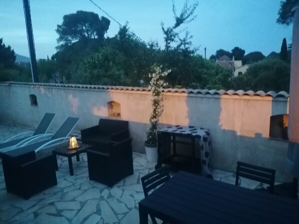 An outdoor patio with lounge chairs, a table, and a potted plant.