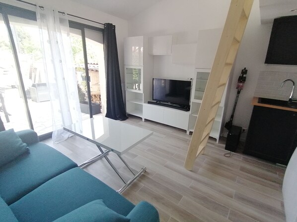 Een moderne woonkamer met een televisie, een glazen tafel en smaragdgroene banken.