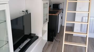 Une cuisine moderne avec des meubles blancs, un four encastré et un four à micro-ondes. Une échelle en bois est adossée au mur, et un téléviseur est fixé au mur.