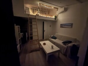 A compact living space with a loft area, a white sofa, a coffee table, and a ladder leading to the loft.