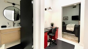 Una habitación de hotel moderna con una puerta negra, un espejo redondo, un escritorio con una silla, una cama y un televisor.