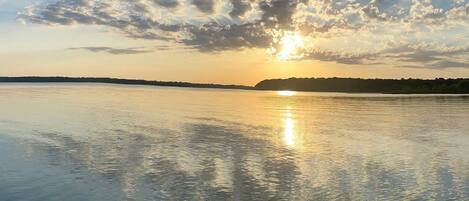 A calm lake with a sunset and clouds reflecting on the water.