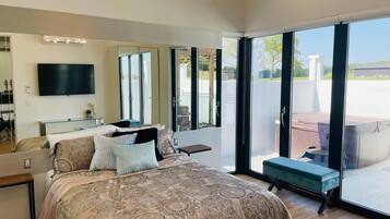 A modern bedroom with a large bed, a TV, and a sliding glass door leading to an outdoor area.
