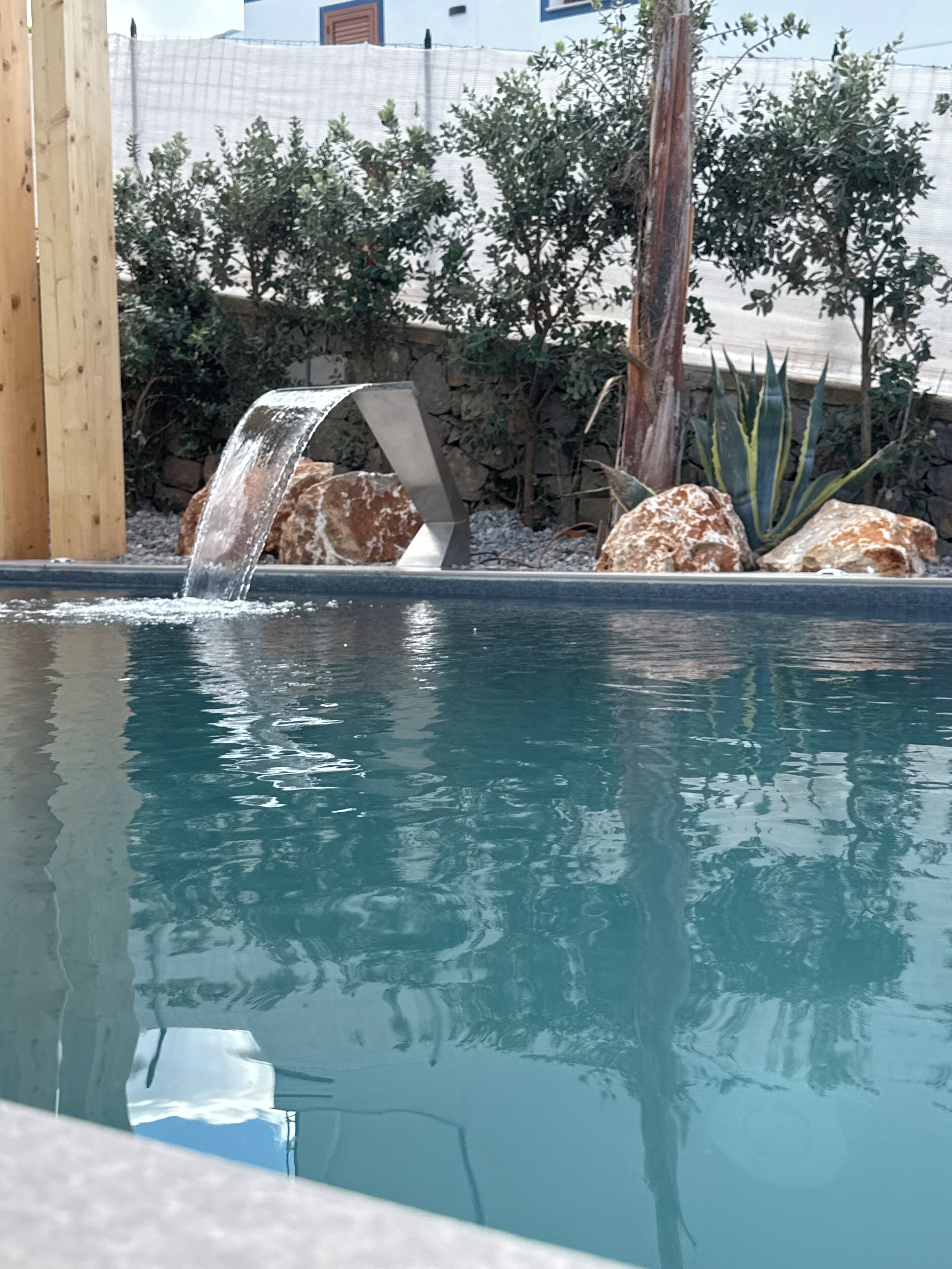A pool with a waterfall feature, surrounded by rocks and plants.