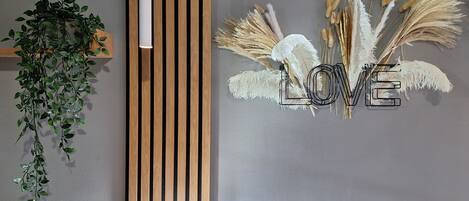 En modern inredning med en vertikal träpanel, en hängande växt och ett väggmonterat dekorativt föremål som stavar ordet ”KÄRLEK” med hjälp av pampasgräs.
