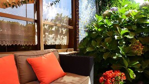 A beige sofa with orange cushions, a green vase with red flowers, and a large green plant.