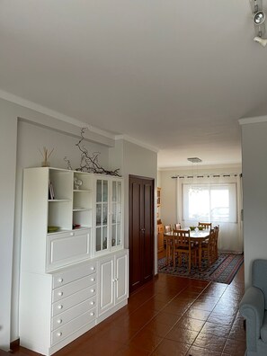 A spacious living area with a dining table, a white cabinet with glass doors, and a patterned rug.