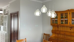 A dining room with a wooden table and chairs, a wooden cabinet with glass doors, and pendant lights.