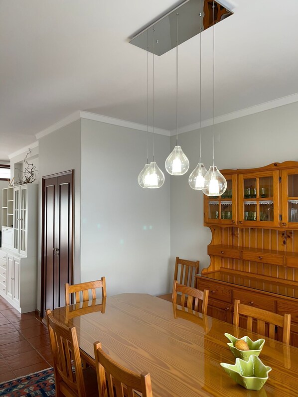 A dining room with a wooden table and chairs, a wooden cabinet with glass doors, and pendant lights.