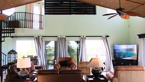 Un vaste espace de vie avec balcon, des canapés en cuir, un téléviseur et un ventilateur de plafond.