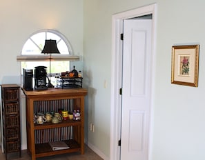 A kitchen with a coffee maker, shelves with jars, a wicker basket, and a white door. - Panoramic Gulf Views | Heated Pool | Beach (Captiva)