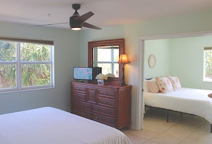 Un dormitorio con cama, cómoda, ventilador de techo, ventana y puerta.