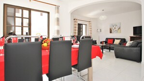 A dining area with a red tablecloth, black chairs, and a fruit basket. There is a sofa and a television in the living area.