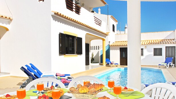 A poolside breakfast setup with a table, chairs, and a pool in the background.