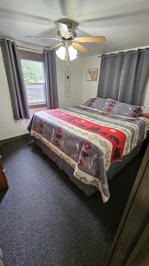 Un dormitorio con cama, ventilador de techo, ventana con cortinas y un adorno en la pared.