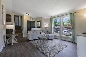 A living room with a sofa, coffee table, and a patterned rug. There is a staircase leading to another room, and a window with curtains. - Columbus: Family Friendly Flat (Columbus)