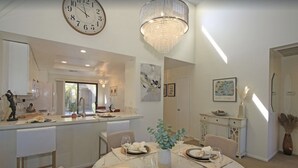Un comedor con una mesa redonda preparada para cuatro, una araña y un reloj en la pared.