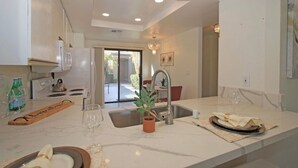 Una cocina moderna con encimera de mármol, pileta de acero inoxidable y un comedor con mesa y sillas.