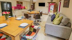 A modern kitchen with white cabinets, a black refrigerator, and a dining area with a wooden table and chairs. - The Stables (Stourbridge)