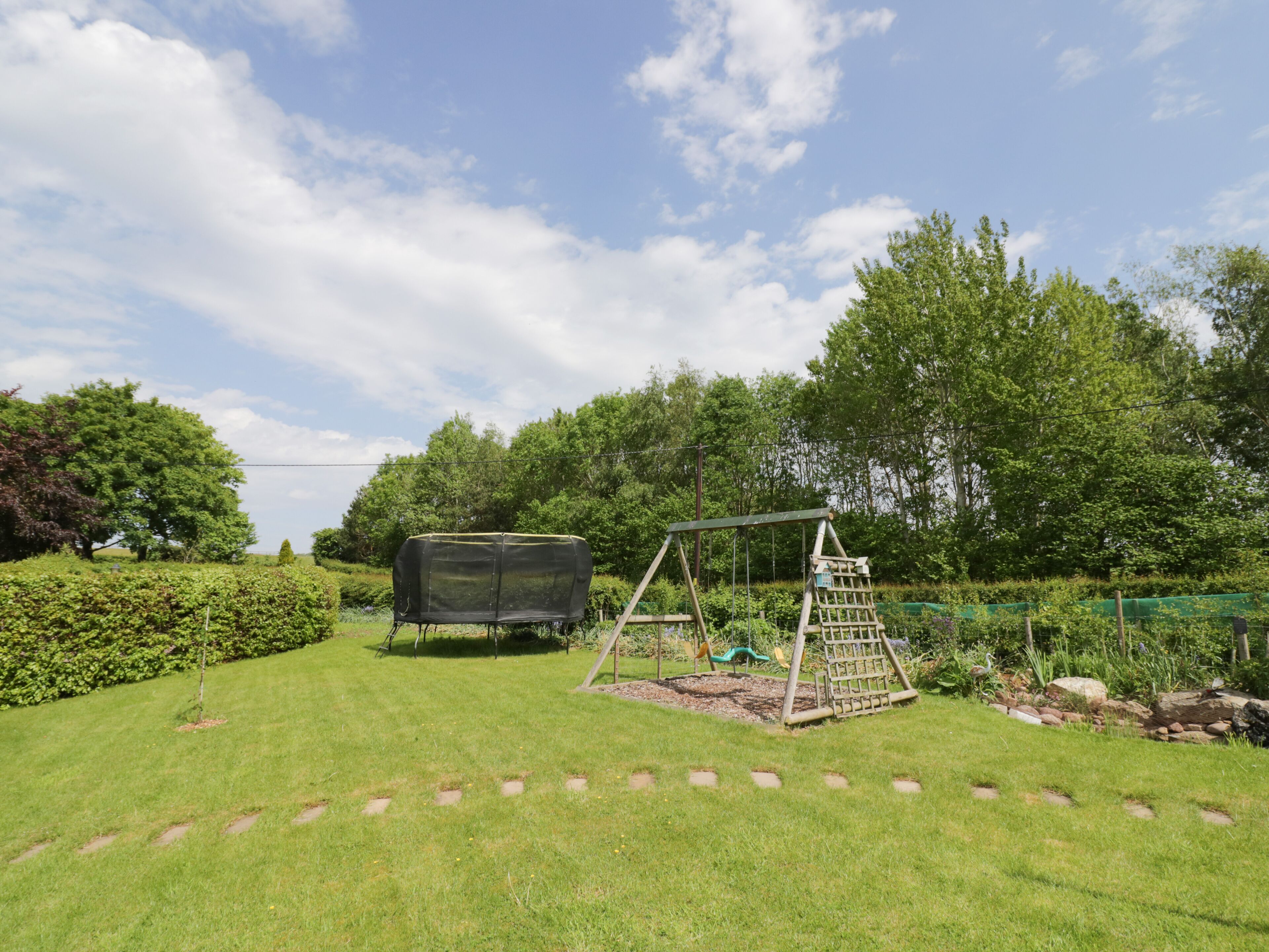 A well-maintained garden with a swing set, a covered play area, and a small pond.