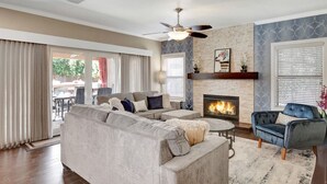 A living room with a fireplace, a ceiling fan, and a large window. - Extravagant Backyard & Dazzling Interior Concepts (Scottsdale)