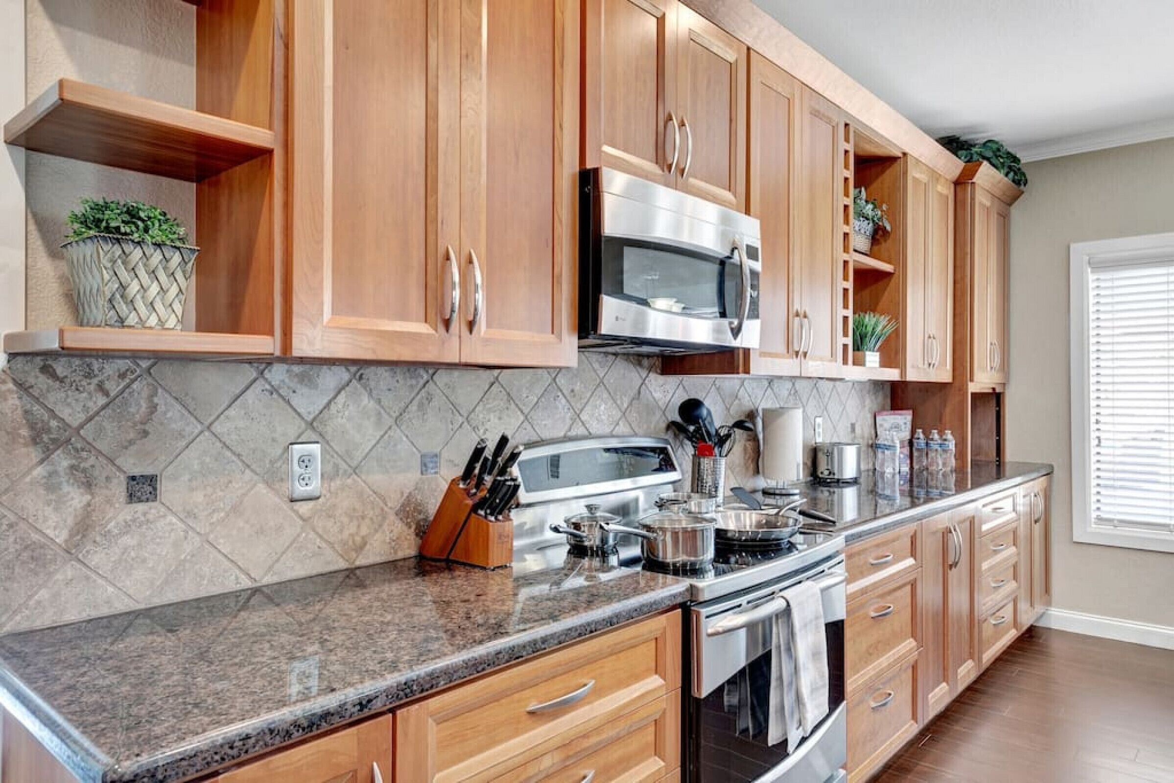 A kitchen with wooden cabinets, a granite countertop, a stainless steel microwave, and a stove.