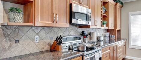 A kitchen with wooden cabinets, a granite countertop, a stainless steel microwave, and a stove.