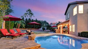 A swimming pool with red umbrellas, lounge chairs, and a house with a barbecue area. - Extravagant Backyard & Dazzling Interior Concepts (Scottsdale)