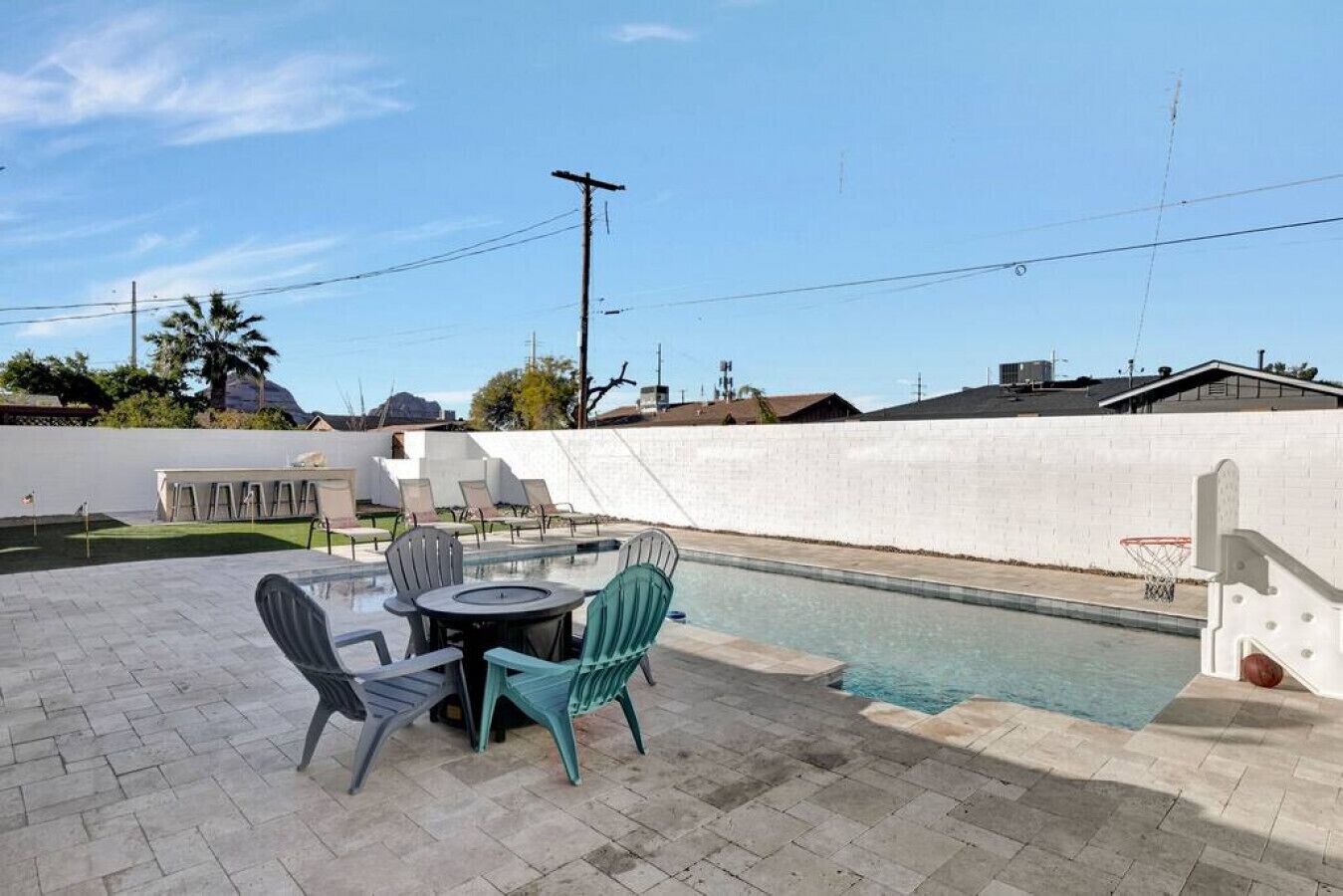 Un espace piscine avec une table et des chaises, un panier de basketball et un mur blanc.
