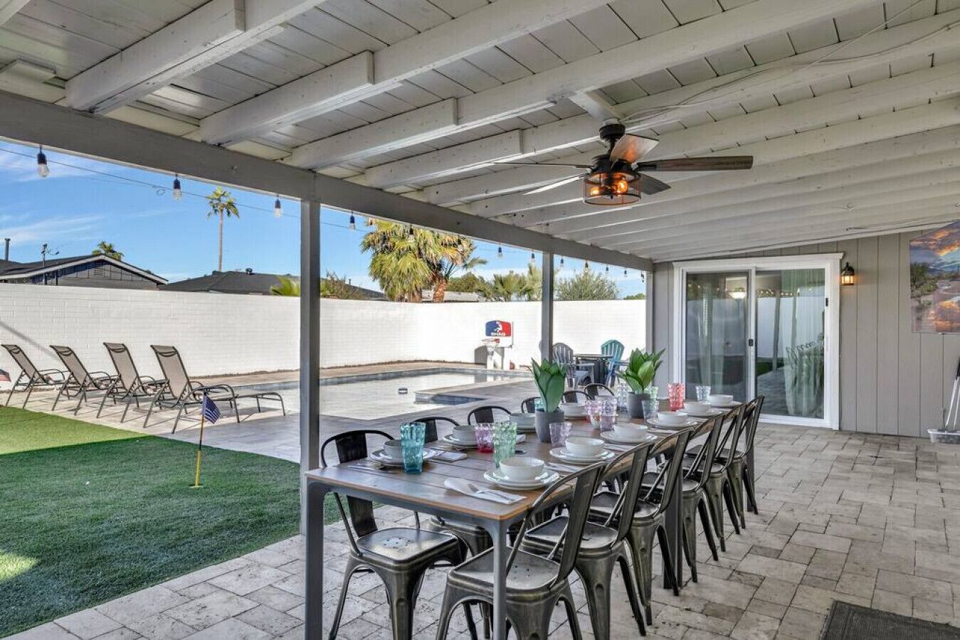 An outdoor patio with a covered dining area, chairs, and a table set for a meal.