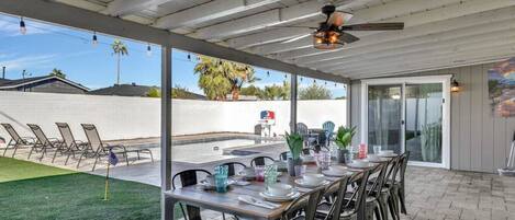 An outdoor patio with a covered dining area, chairs, and a table set for a meal.