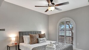 Une chambre à coucher comprenant un lit, une table de chevet, un ventilateur de plafond et une fenêtre avec des stores.