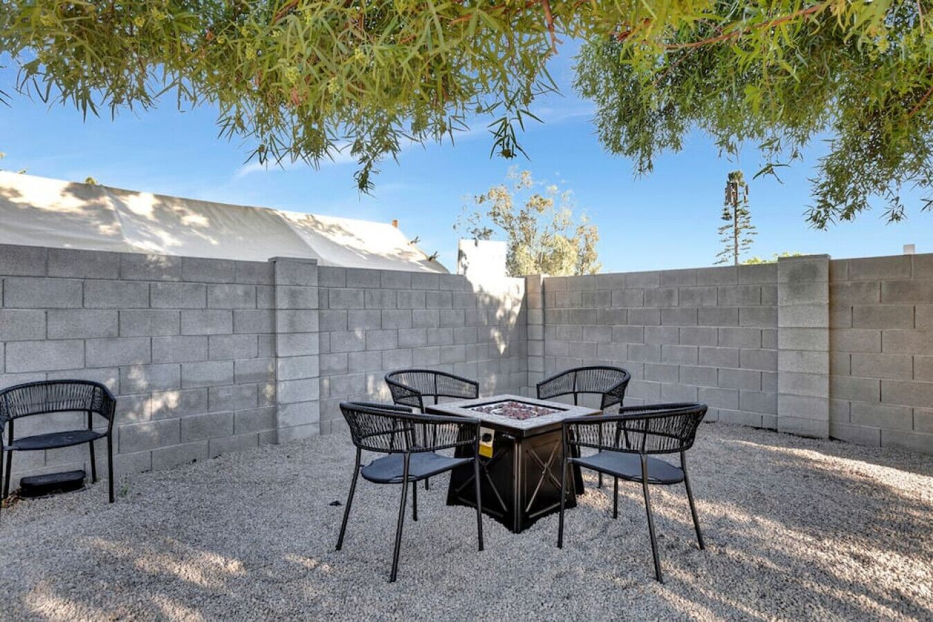 An outdoor patio with a table and chairs, surrounded by a concrete wall and gravel ground.